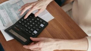 木のテーブルの上で大きめの電卓と書類を確認する手元。家族の2Pモードや予算・ポイント設計のイメージに最適。
