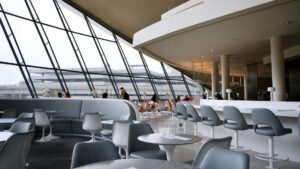大きな窓から滑走路を望む明るい空港ラウンジの内装。モダンな椅子とテーブルが並び、利用客が静かに過ごしている。