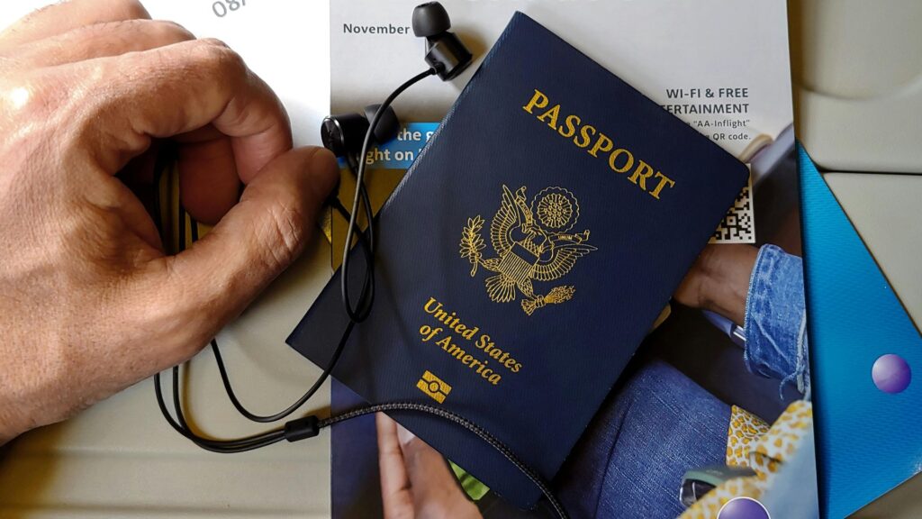 機内のトレーテーブルで、米国パスポートと有線イヤホン、Wi-Fi案内のパンフレットを手元に置いている様子