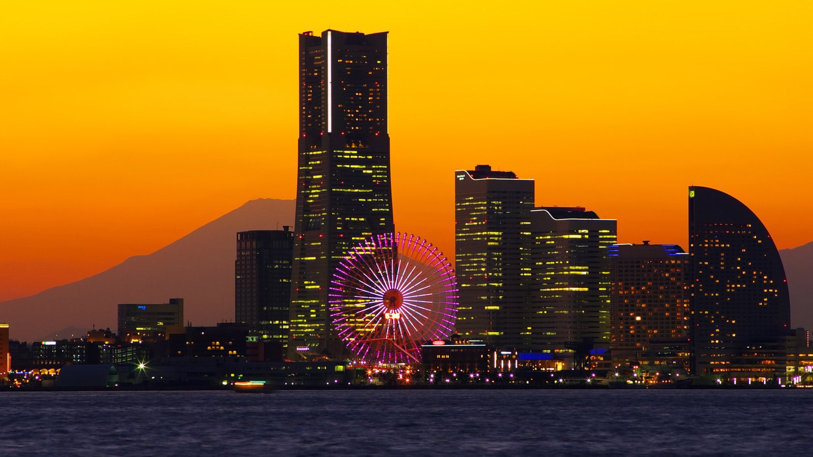 夕焼けの空に富士山のシルエットが浮かび、手前に横浜ランドマークタワーや観覧車が光るみなとみらいの夜景